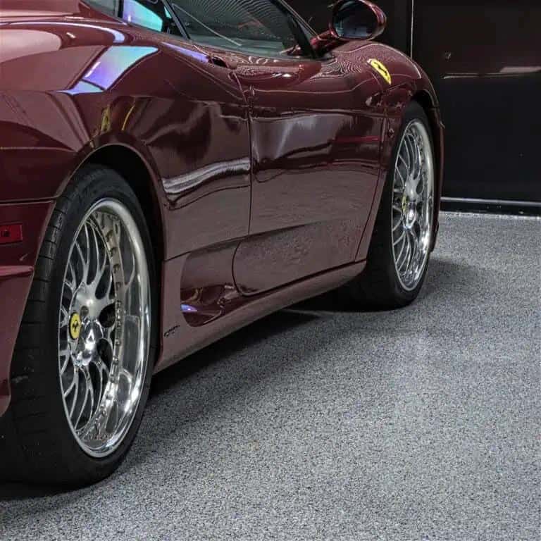 Red sports car parked atop a gray, full flake epoxy and polyaspartic coated concrete floor. 