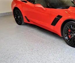 Red sports car parked atop a full flake polyaspartic coating in a garage.